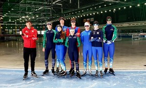 Zdjęcie przedstawia zawodników łyżwiarstwa szybkiego wraz z trenerami na arenie lodowej w Tomaszowie Mazowieckim